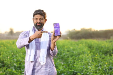 Happy rural Indian farmer pointing at the screen of his smart phone, showing his mobile phone's...