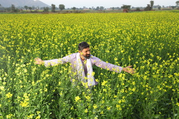 Happy Indian farmer enjoying the wind standing in the field spreading his arms and looking up in the sky.