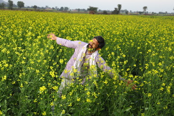 Happy Indian farmer enjoying the wind standing in the field spreading his arms and looking up in the sky.