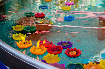 Sacrificial candles in the form of lotus flowers float in a container with water near the Buddha statue on the holiday of Buddha Purnima