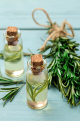 Natural rosemary essential oil in a glass bottle and a fresh sprig of rosemary on a blue table. face and body skin care. spa.