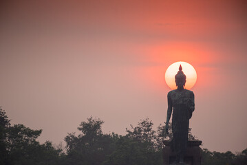 Stand big tall walk Buddha Statue in sun set Light background in park of thailand temple.Yellow...