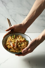 Man's hand holds a bowl with healthy Thai chicken noodle salad. Fresh and cold boiled rice noodles with chicken and vegetables. Aisan cuisine. White background.