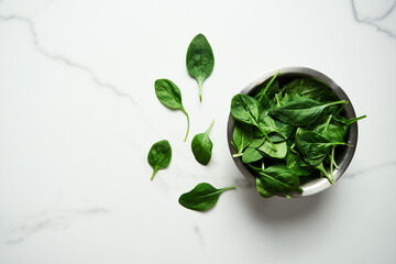 A bunch of Fresh baby spinach leaves in the in a stainless steel bowl on white marble background.Flat lay, top view with copy space