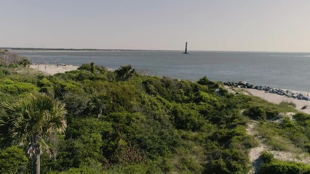 Morris Island Lighthouse in Charleston South Carolina on water by Folly Beach - Drone approaching over palm trees and bushes on beach