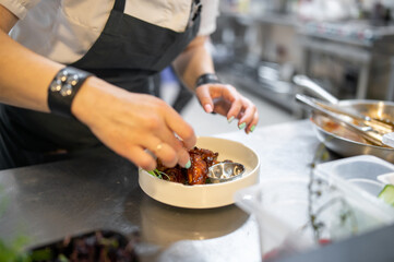 woman chef cooking chicken wings in a sauce in the kitchen