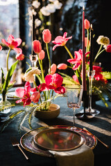 Festive dinner table is served dishes and cutlery and decorated with flowers tulips and greenery, candles. Birthday celebration. Family holidays in modern dining room. Stylish spring party. Wedding.