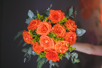 A woman hand holding an orange bouquet of roses