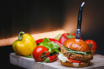 A vegetarian burger with falafel and a knife on it and a tomato on the side