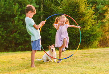Children playing with pet dog jumping through hula hoop - obrazy, fototapety, plakaty