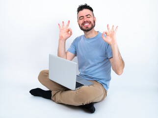 Young caucasian man with laptop sitting over white studio relax and smiling with eyes closed doing meditation gesture with fingers. Yoga concept.