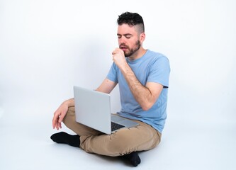 Young caucasian man with laptop sitting over white studio feeling unwell and coughing as symptom for cold or bronchitis. Healthcare concept.