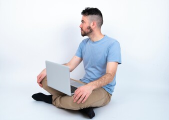 Close up side profile photo Young caucasian man with laptop sitting over white studio not smiling attentive listen concentrated