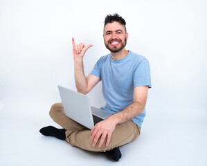 Young caucasian man with laptop sitting over white studio showing up number six Liu with fingers gesture in sign Chinese language