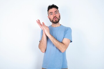 Surprised emotional Young caucasian man wearing blue T-shirt over white background rubs palms and stares at camera with disbelief