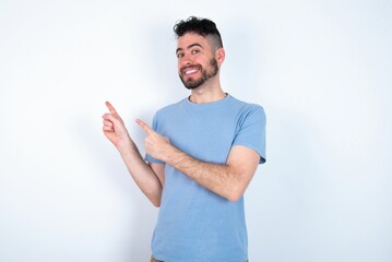 Young caucasian man wearing blue T-shirt over white background points at copy space indicates for...