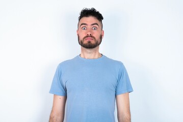 Stunned Young caucasian man wearing blue T-shirt over white background stares reacts on shocking news. Astonished man holds breath