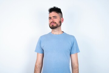 Displeased Young caucasian man wearing blue T-shirt over white background frowns face feels unhappy...