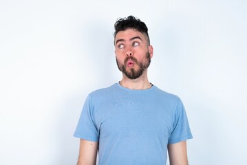 Shocked Young caucasian man wearing blue T-shirt over white background look empty space with open mouth screaming: Oh My God! I can't believe this.