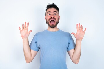 Fototapeta premium Delighted positive Young caucasian man wearing blue T-shirt over white background opens mouth and arms palms up after having great result