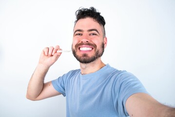 Fototapeta premium Young caucasian man wearing blue T-shirt over white background make selfie holding an invisible braces aligner, recommending this new treatment. Dental healthcare concept.