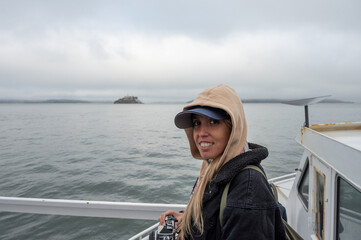 Portrait of a young girl in a cap and hood with her photo camera on the boat sailing through the sea towards the island of Alcatraz