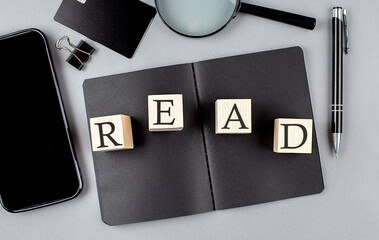 Word READ on wooden block on black notebook with smartpone, credit card and magnifier