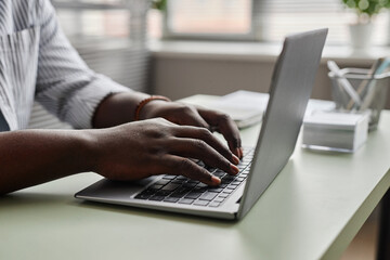 Close up of unrecognizable black man working online , focus on male hands typing at laptop keyboard