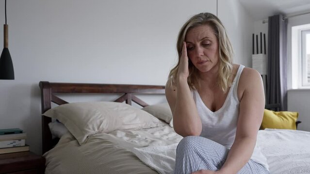 Menopausal Mature Woman Suffering With Low Mood And Anxiety Sitting On Bed At Home 