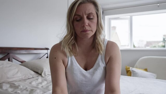 Menopausal Mature Woman Suffering With Low Mood And Anxiety Sitting On Bed At Home 