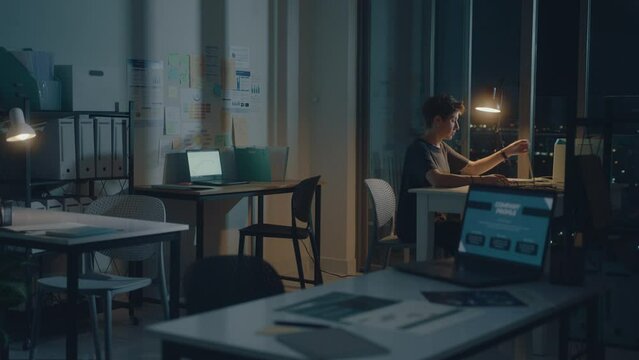 Young woman staying late at work, turning off laptop and desk lamp, leaving the office last at night. Overworking concept