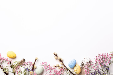 Easter composition with spring flowers and colorful quail eggs over white background. Springtime and Easter holiday concept with copy space. Top view