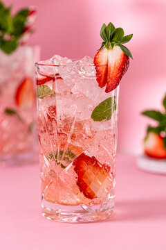 Fresh healthy limonate cocktail with crushed ice, strawberry and mint on pinkbackground. Summer cold drink concept