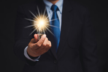 Businessman in a suit holds a light bulb while standing on a black background