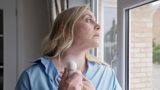 Menopausal Mature Woman Having Hot Flush At Home Cooling Herself With Handheld Electric Fan 