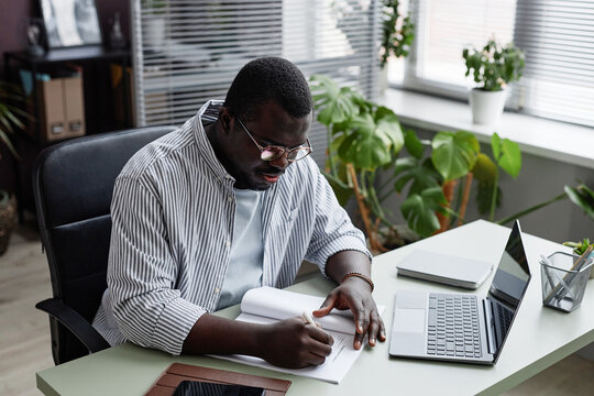 Portrait Of Adult Black Man Wearing Glasses And Signing Documents At Workplace In Casual Office Setting