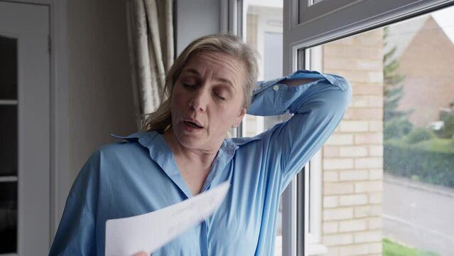 Menopausal Mature Woman Having Hot Flush At Home Cooling Herself With Letters Or Documents