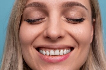 Obraz premium close-up of a woman with a snow-white Hollywood smile and closed eyes on a blue background