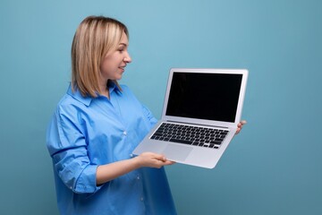 smart attentive young woman in a casual shirt holding a laptop with a mockup in her hands on a blue isolated background with copy space