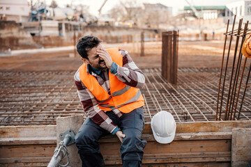 A site worker is sitting on concrete foundation and touching his painful leg.