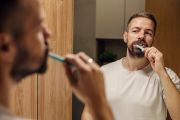 Reflection of a man brushing his teeth in a bathroom.