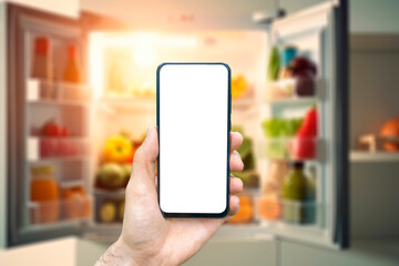 Online grocery delivery app in a mobile phone. The men is holding a phone in his hand opposite the refrigerator.Food market service in smartphone. Grocery shopping background concept.