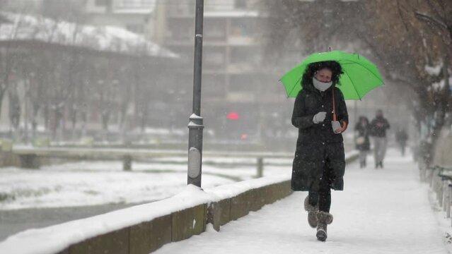 Slow motion of a happy woman holding umbrella and running in a park under heavy snow and enjoying the snowy day