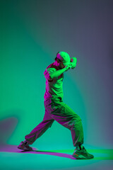 Fashionable handsome professional dancer man in fashion clothes dancing and adjusting his cap in a creative studio with cyan and magenta light