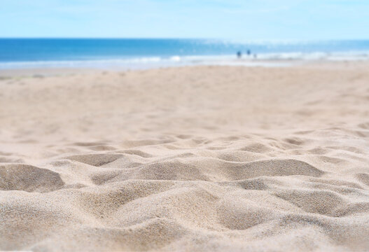 A coastal foreground texture scene to place products on the sand with a blurred sea background on a sunny summer day.
