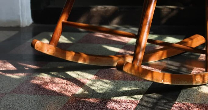 The rocking chair rocks or moves in the room. The sun shines on the rocking chair for elderly people. It is comfortable furniture.