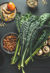 Tuscan kale leaves on kitchen table with nuts, mushrooms and other healthy ingredients for tasty vegan food cooking, top view