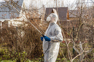 Using chemicals in the garden orchard gardener applying an insecticide a fertilizer to his fruit shrubs, using a sprayer