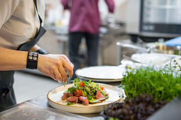 chef hand cooking Roast beef salad with vegetables on restaurant kitchen