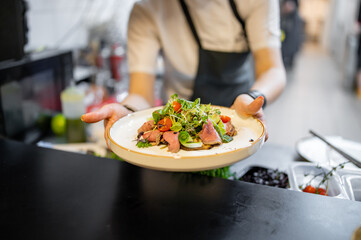 chef hand cooking Roast beef salad with vegetables on restaurant kitchen